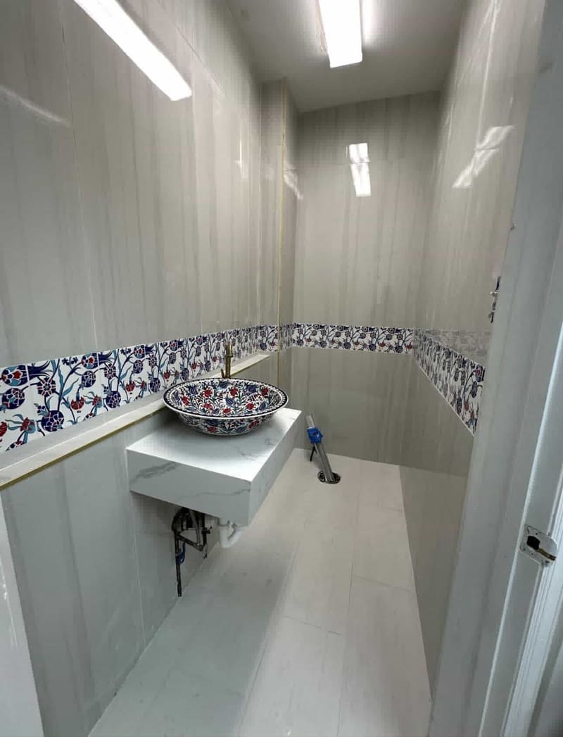 Powder room with large porcelain wall panels, a blue and red floral tile border and a floating marble-look vanity with a painted vessel sink