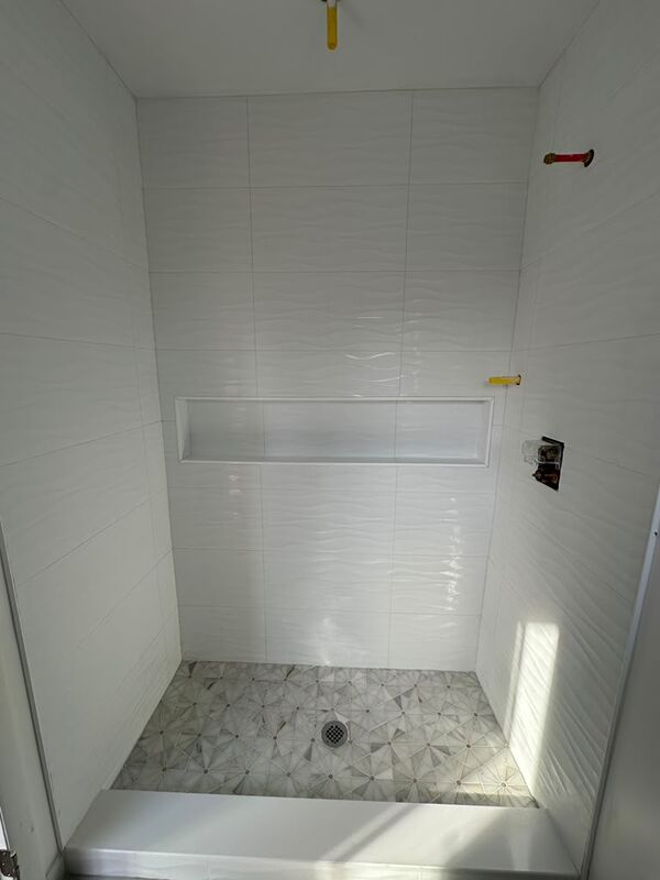 Walk-in shower with large white wave-relief wall tile, a full-width recessed niche and a grey and white patterned marble mosaic floor